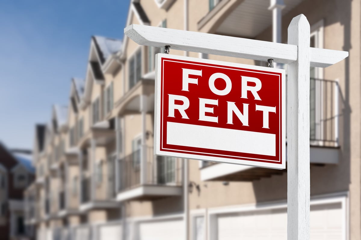 For rent sign in front of a row of apartment buildings with balconies and garages