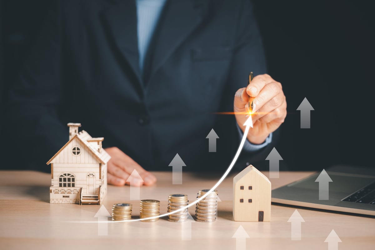 Businessman drawing a rising arrow over coins and house models, illustrating real estate investment growth